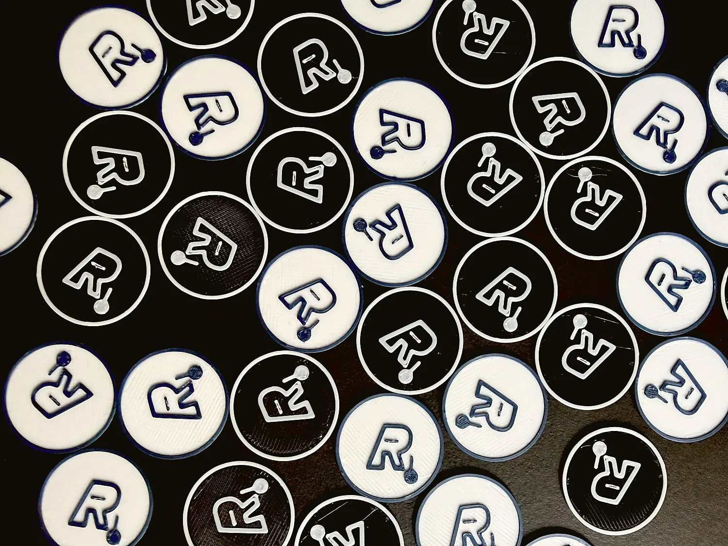 Zahlreiche 3D-gedruckte Logo-Siegel in Schwarz und Weiß, nebeneinander